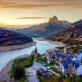 Un pueblo de piedra con tejados azules a orillas de un embalse, bajo un pico montañoso imponente. Un ejemplo de los pueblos mas bonitos de Huesca.