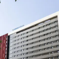 Edificio moderno con el logo "ILUNION Hotels" en la parte superior. Fachada gris con ventanas y detalles rojos.