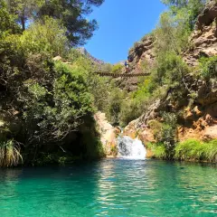 Un puente colgante cruza un **río verde** en Granada, con una cascada y vegetación exuberante.