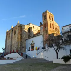 Iglesia de la Asunción en Cazalla de la Sierra, con su torre campanario y fachadas de piedra y cal bajo un cielo azul.