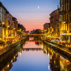 Atardecer en los Navigli de Milán, con gente paseando y luces reflejándose en el canal.