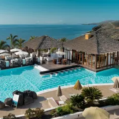 Un resort todo incluido con piscinas cristalinas, palmeras y vistas al mar. Mesas al aire libre y un bar acuático invitan a relajarse bajo el sol.