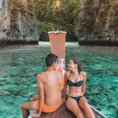 Pareja en bote de madera, aguas cristalinas y acantilados. Un destino ideal para saber donde viajar en enero.