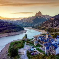 Un pueblo de piedra con tejados azules a orillas de un embalse, bajo un pico montañoso imponente. Un ejemplo de los pueblos mas bonitos de Huesca.