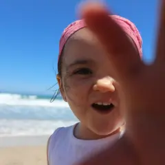 Niña con bandana rosa y arena en la cara, disfrutando de sus viajes con niños en la playa.