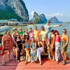 Grupo de amigos disfrutando en un barco en Tailandia, con islas kársticas al fondo. ¡Parece la mejor época para viajar a Tailandia!