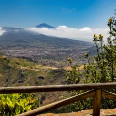 Vista panorámica desde Anaga, Tenerife, con el Teide asomando entre las nubes. Un paisaje verde y montañoso se extiende hasta el mar.