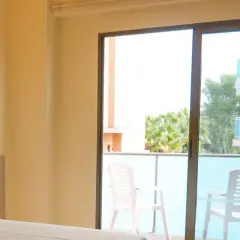 Habitación con balcón y vistas a palmeras en el hotel htop molinos park. Dos sillas de plástico blanco esperan en el balcón.