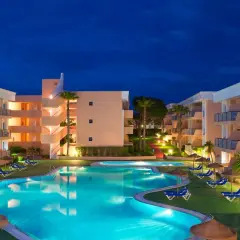 Resort con piscina iluminada y edificios de apartamentos bajo el cielo nocturno. Un lugar perfecto para disfrutar del sol Sancti Petri.