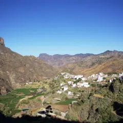 Pueblo blanco de Tejeda, Gran Canaria, con montañas escarpadas y campos verdes en un día soleado.