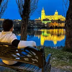 Persona sentada en un banco contempla la Catedral de Salamanca iluminada al anochecer, reflejada en el río. Ideal para saber qué ver en Salamanca en un día.