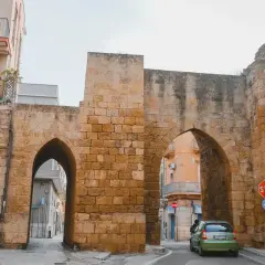 Antigua puerta de piedra con arcos, un coche verde pasa. Un lugar perfecto para un brindis por la historia.