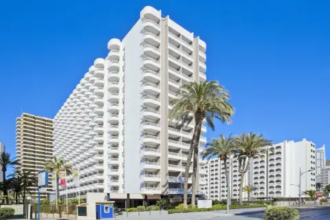 Edificio Sol con balcones curvos y palmeras bajo un cielo azul.