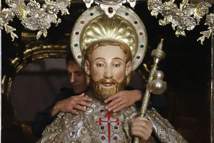 Un hombre ajusta una figura religiosa adornada, quizás preparándola para una celebración que se celebra hoy en España.