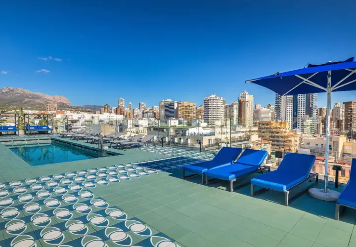Terraza con piscina y tumbonas azules en Barceló Benidorm, con vistas a la ciudad y montañas.