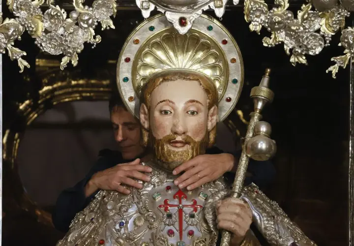 Un hombre ajusta una figura religiosa adornada, quizás preparándola para una celebración que se celebra hoy en España.