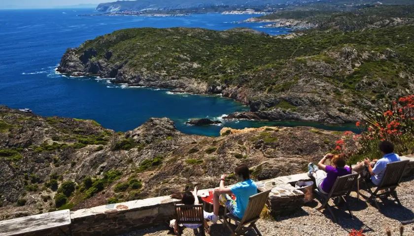 Disfrutando de la vista del Cap de Creus, con sus calas y montañas, mientras la gente descansa en sillas.