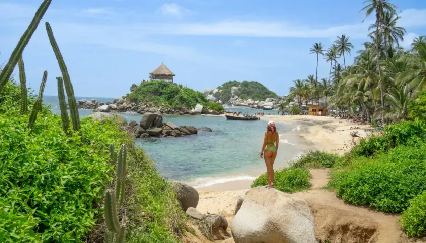 Mujer en bikini admira una playa paradisíaca con palmeras y un kiosko en una isla, ideal para un viaje a Colombia.