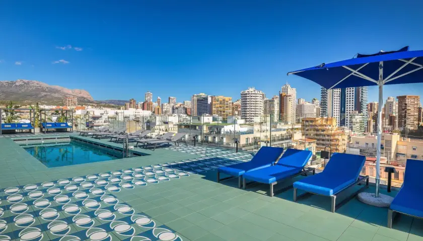 Terraza con piscina y tumbonas azules en Barceló Benidorm, con vistas a la ciudad y montañas.