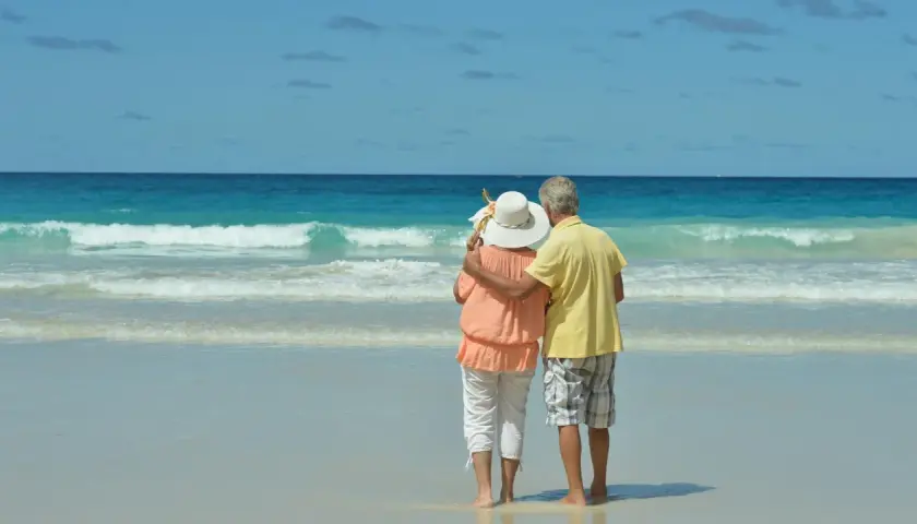 Pareja mayor disfrutando de sus viajes El Corte Inglés mayores 60 años en una playa paradisíaca.