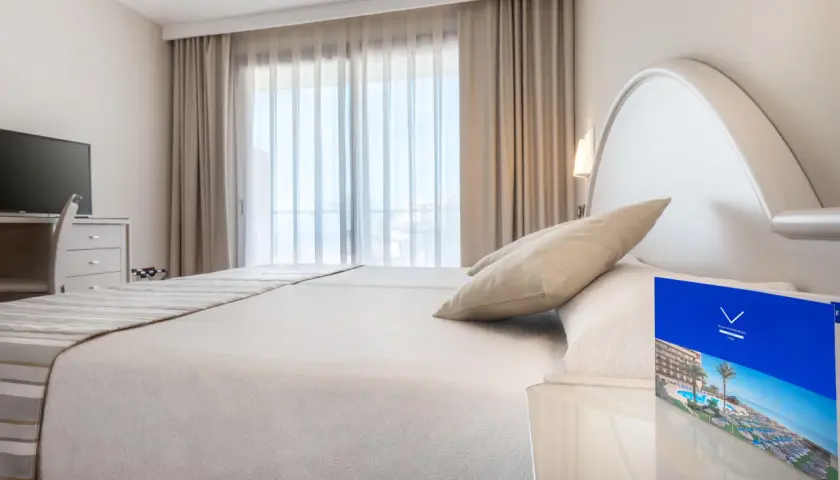 Habitación luminosa con cama doble, TV y folleto del Vik Gran Hotel Costa del Sol.