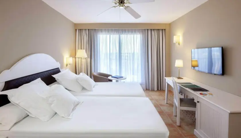 Habitación doble con camas blancas y escritorio en el hotel Occidental Isla Cristina.