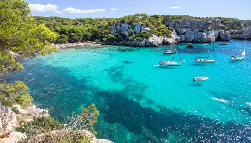 Calas turquesas y veleros, ideal para saber qué ver en Menorca en 3 días. Disfruta de playas paradisíacas y acantilados verdes.