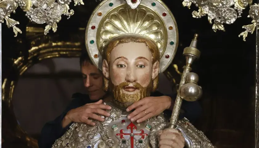 Un hombre ajusta una figura religiosa adornada, quizás preparándola para una celebración que se celebra hoy en España.