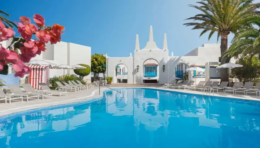 Piscina azul brillante y tumbonas bajo palmeras en el hotel Riu Oliva Beach Resort.