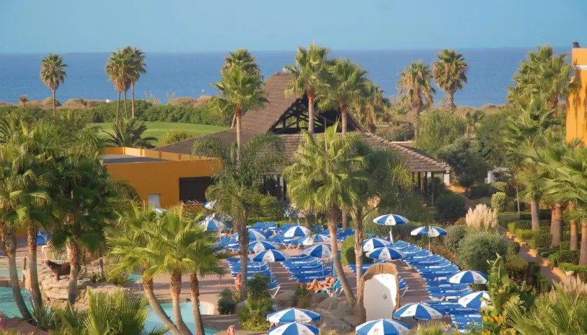 Vista aérea del hotel Playa Ballena con palmeras, piscinas y tumbonas bajo sombrillas azules y blancas.