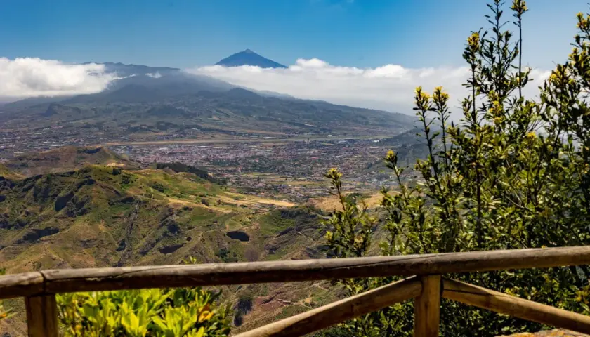 Vista panorámica desde Anaga, Tenerife, con el Teide asomando entre las nubes. Un paisaje verde y montañoso se extiende hasta el mar.