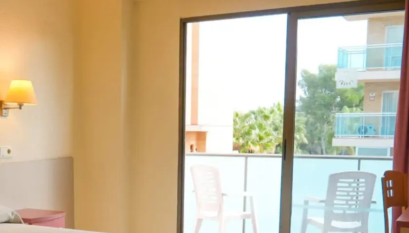 Habitación con balcón y vistas a palmeras en el hotel htop molinos park. Dos sillas de plástico blanco esperan en el balcón.