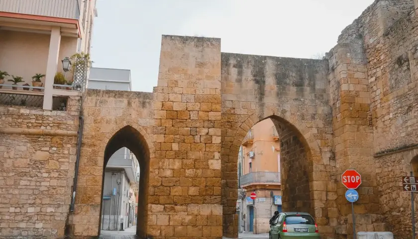 Antigua puerta de piedra con arcos, un coche verde pasa. Un lugar perfecto para un brindis por la historia.