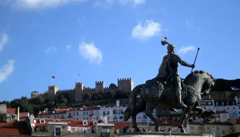 Estatua ecuestre de un rey con el Castillo de San Jorge al fondo, un lugar que ver en Lisboa.