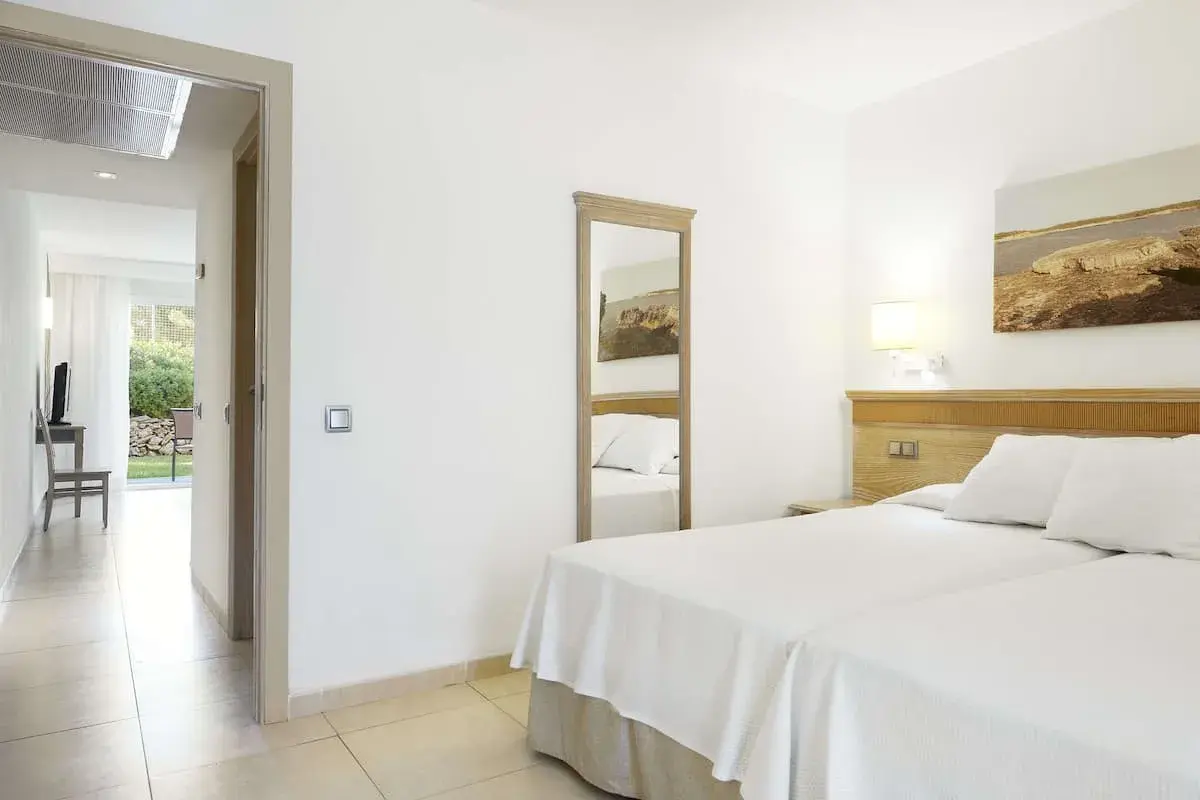 Habitación luminosa en Iberostar Club Cala Barca con dos camas, espejo de cuerpo entero y acceso a un patio exterior.
