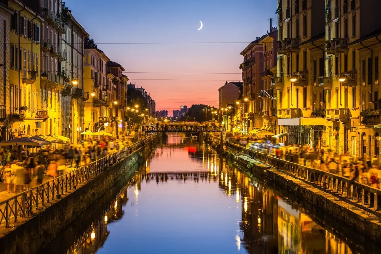 Atardecer en los Navigli de Milán, con gente paseando y luces reflejándose en el canal.