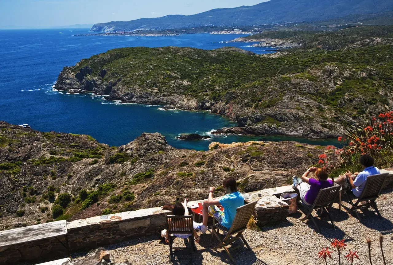 Disfrutando de la vista del Cap de Creus, con sus calas y montañas, mientras la gente descansa en sillas.