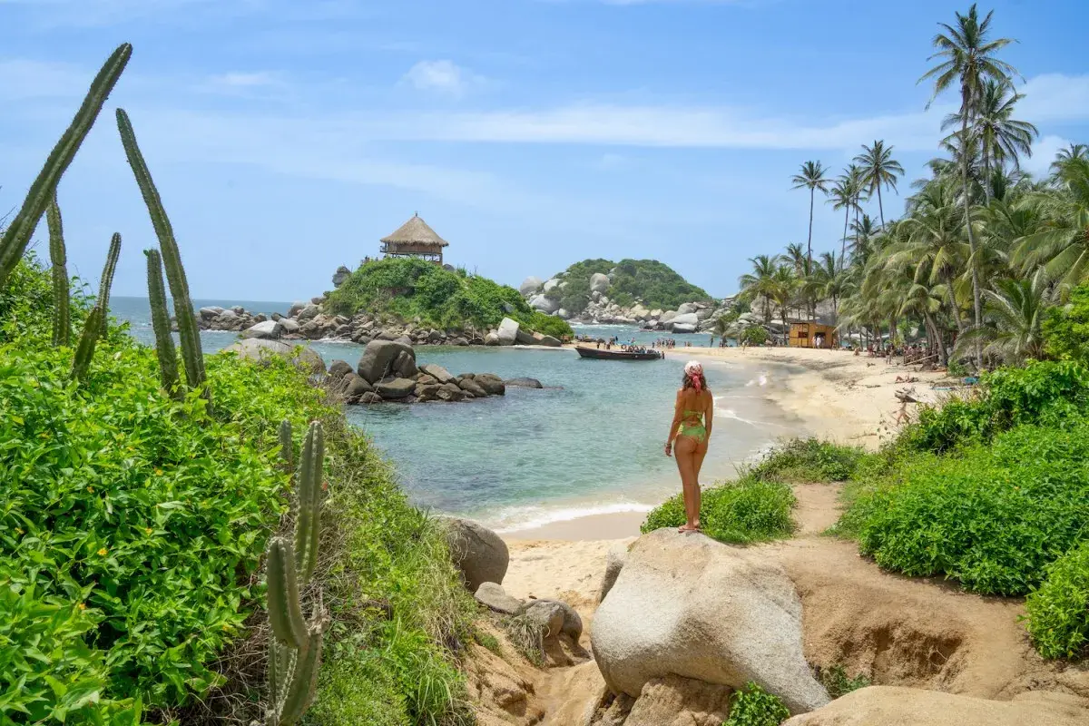 Mujer en bikini admira una playa paradisíaca con palmeras y un kiosko en una isla, ideal para un viaje a Colombia.