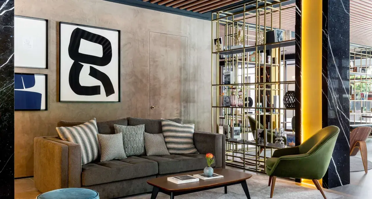 Sofá gris con cojines decorativos, mesa de centro y estantería dorada en un lobby de Radisson Collection.