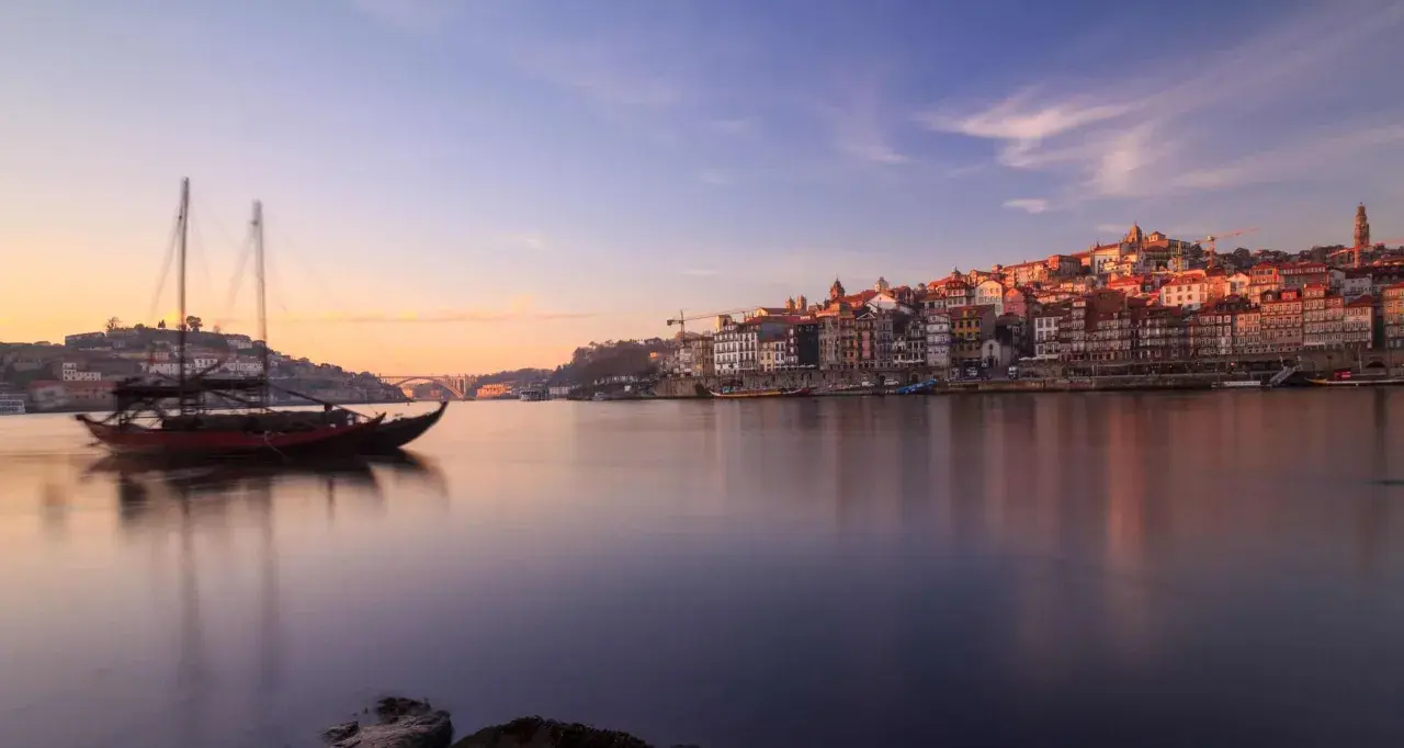 Barcos tradicionales navegan por el río Duero al amanecer, con la pintoresca ciudad de Oporto al fondo. Un lugar imprescindible que ver en el norte de Portugal.