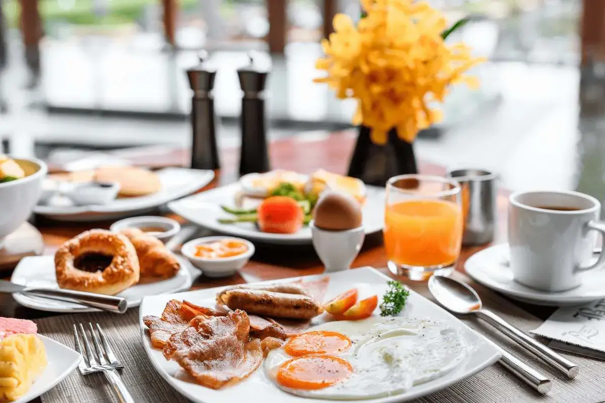 Desayuno abundante con huevos, salchichas, tocino y zumo de naranja, perfecto para tus viajes fin de semana baratos todo incluido.