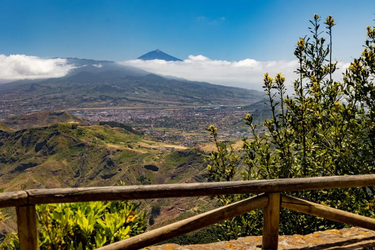 Vista panorámica desde Anaga, Tenerife, con el Teide asomando entre las nubes. Un paisaje verde y montañoso se extiende hasta el mar.