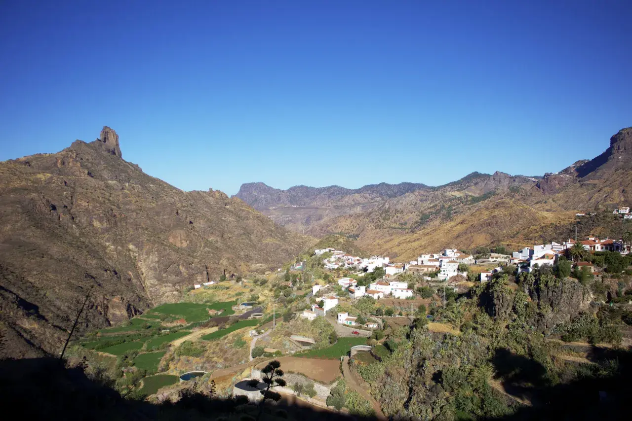 Pueblo blanco de Tejeda, Gran Canaria, con montañas escarpadas y campos verdes en un día soleado.