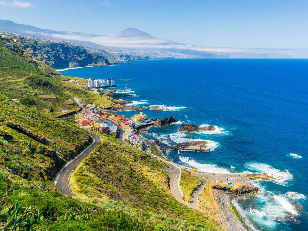 Costa de Tenerife con pueblo colorido, mar azul y el Teide al fondo. ¡Perfecto para tus viajes a Tenerife todo incluido 2x1!