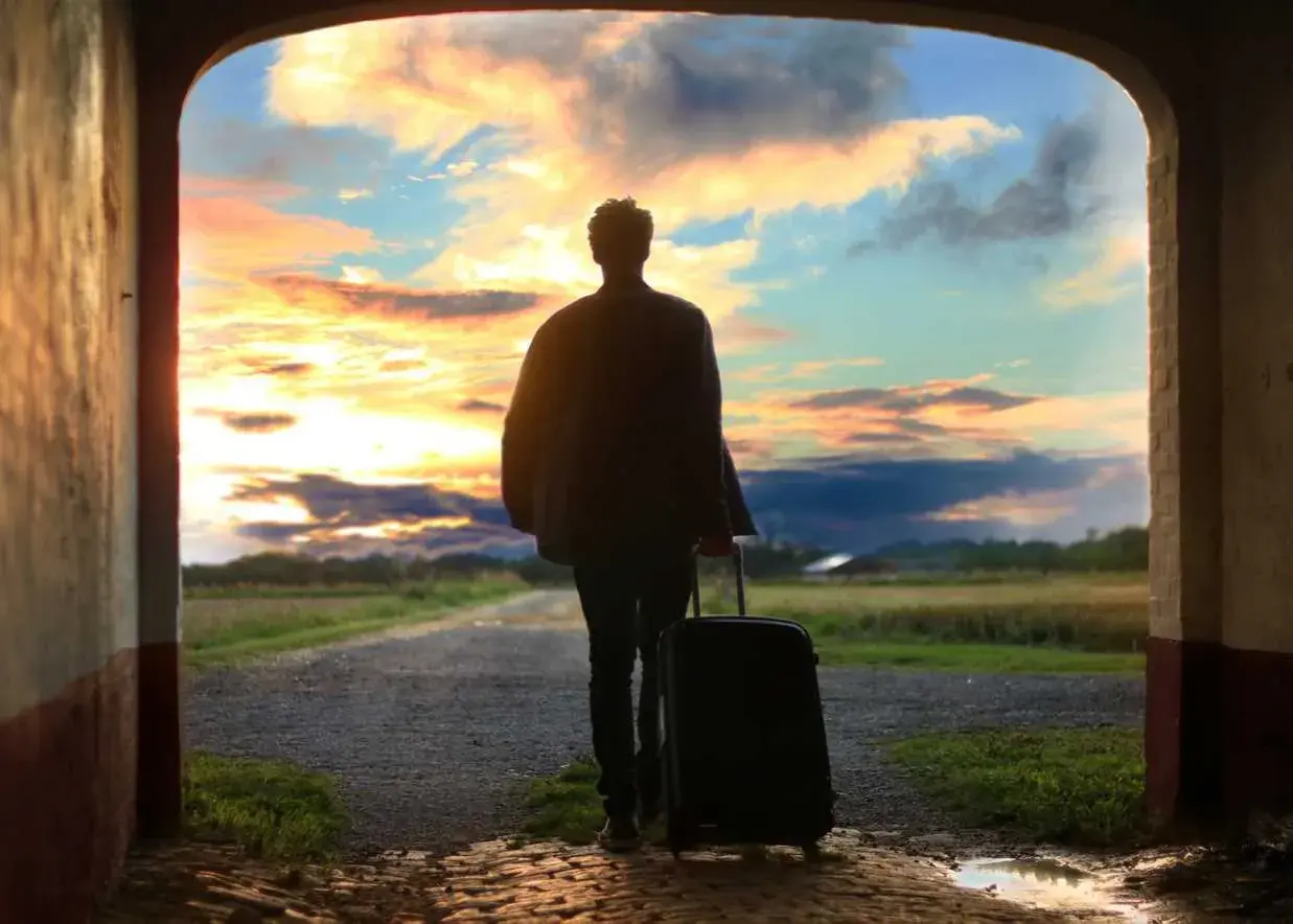 Persona con maleta, lista para viajar, ante un atardecer espectacular. ¡Aprovecha las ofertas viajes última hora 2x1!