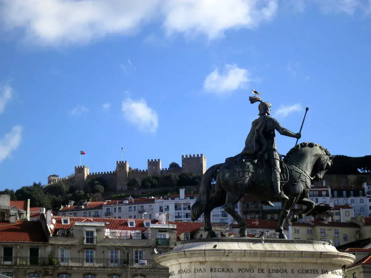 Estatua ecuestre de un rey con el Castillo de San Jorge al fondo, un lugar que ver en Lisboa.
