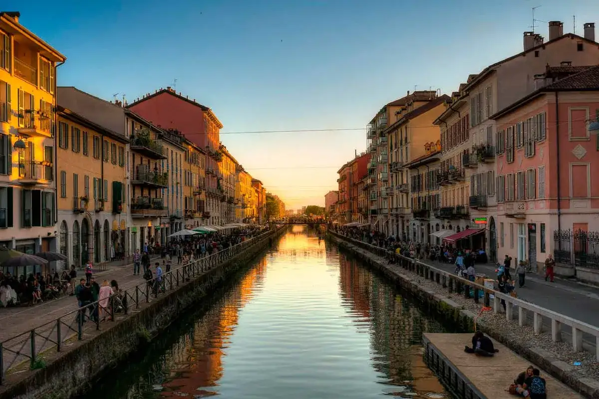 Atardecer dorado en los Navigli de Milán, con gente paseando y disfrutando de las terrazas junto al canal.