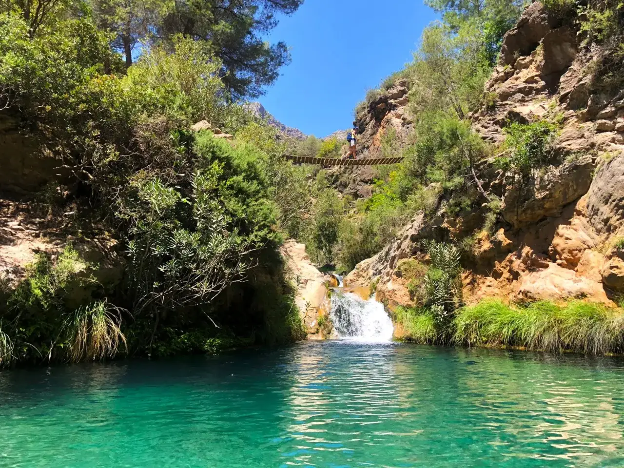 Un excursionista cruza un puente colgante sobre un río verde en un cañón rocoso cerca de Granada.