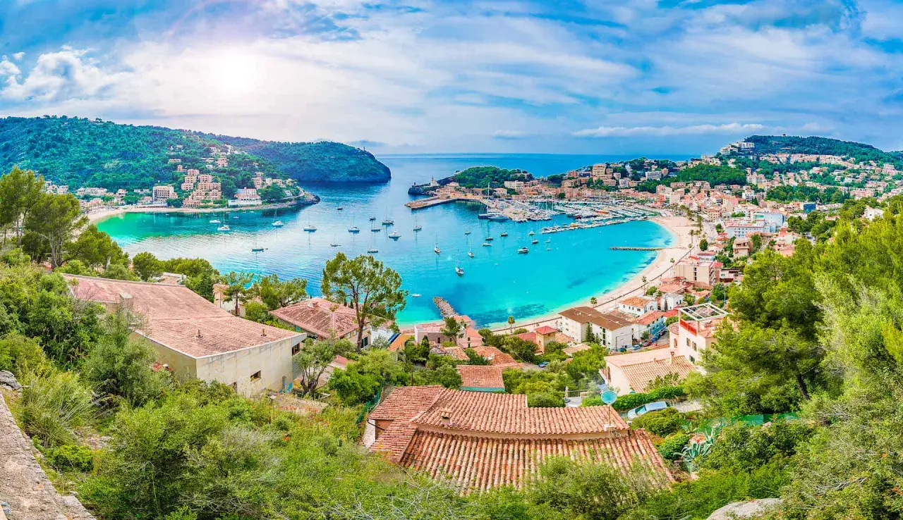 Bahía de Mallorca con aguas turquesas, barcos y casas blancas. Un paisaje que recuerda a Barcelona por su encanto mediterráneo.