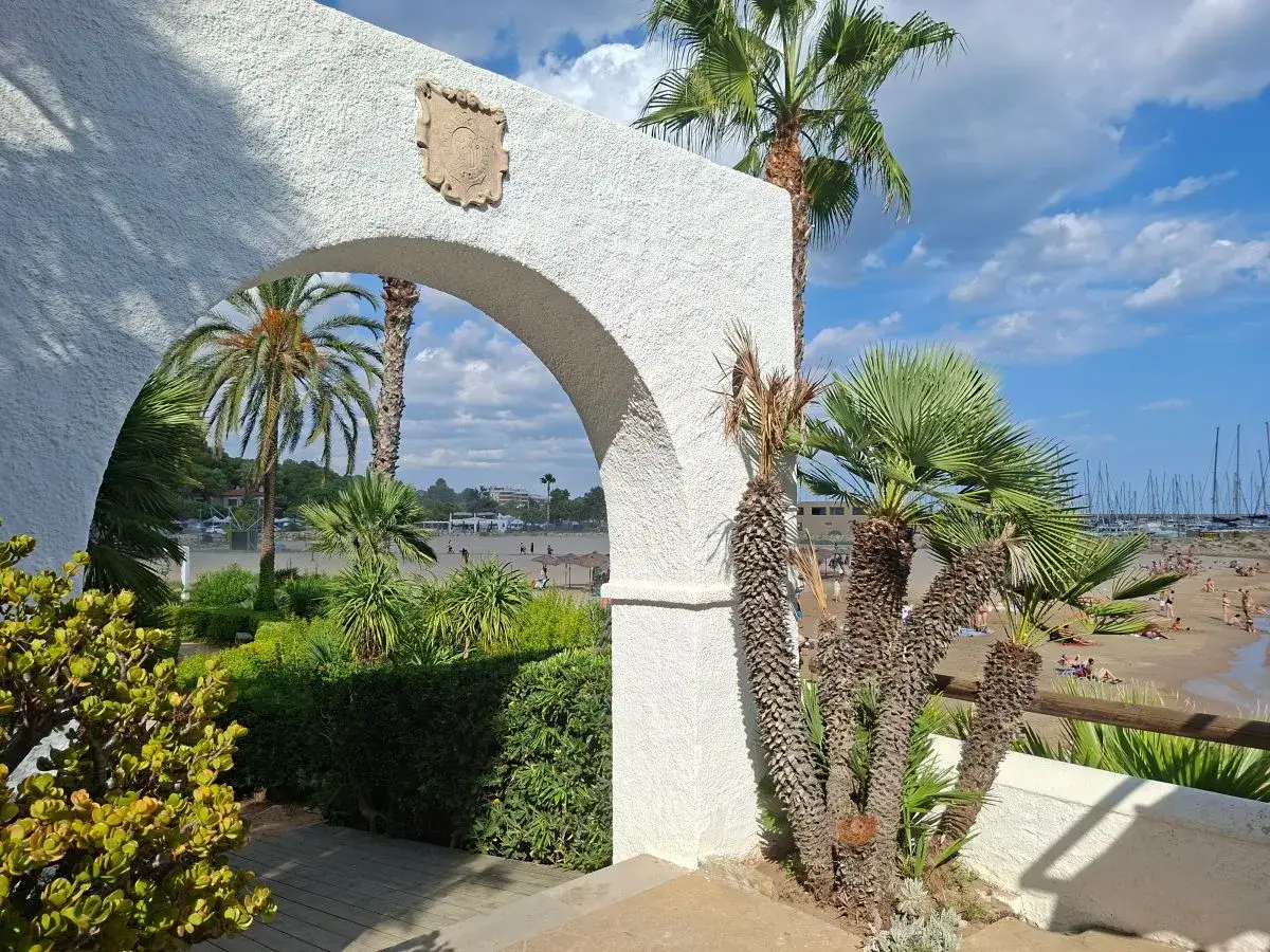 Vista de una playa con palmeras y veleros a través de un arco blanco. El sol brilla en un día perfecto para la roda de bara.